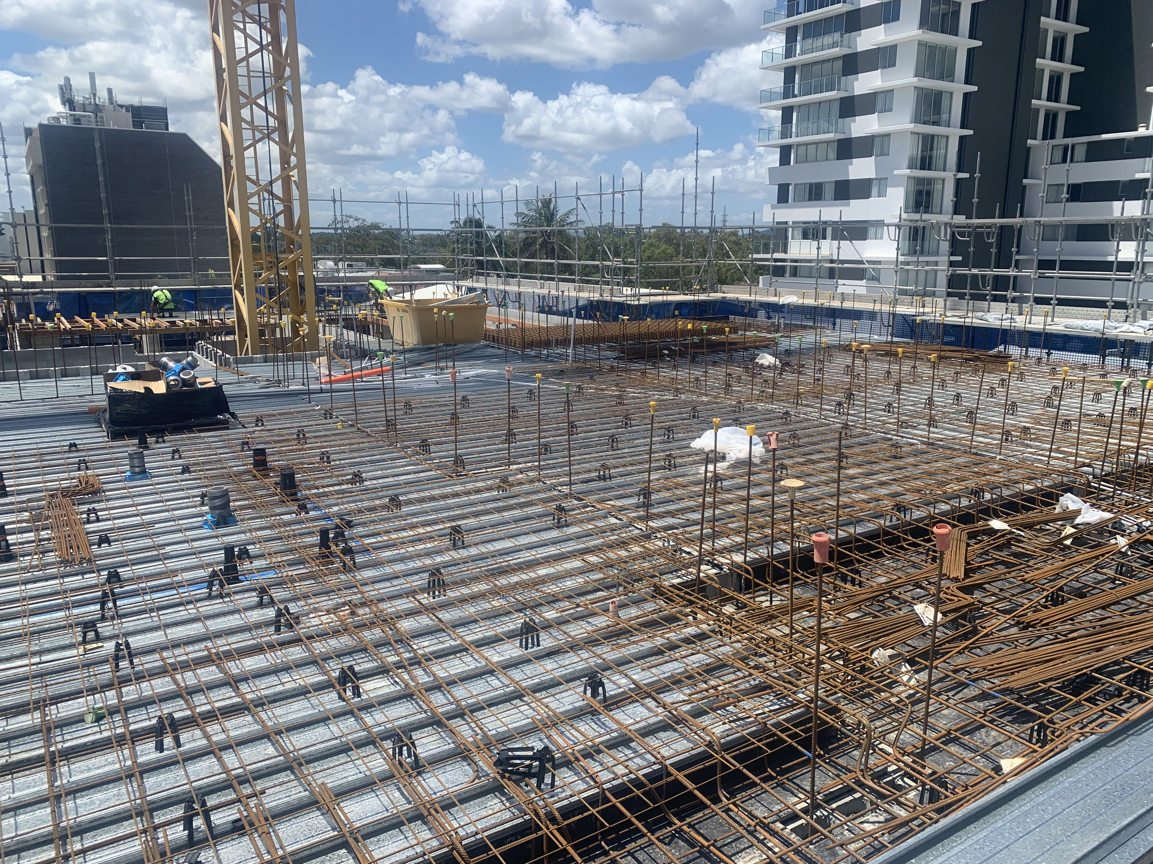 High-rise building concrete slab preparation — workers and crane with apartment towers behind