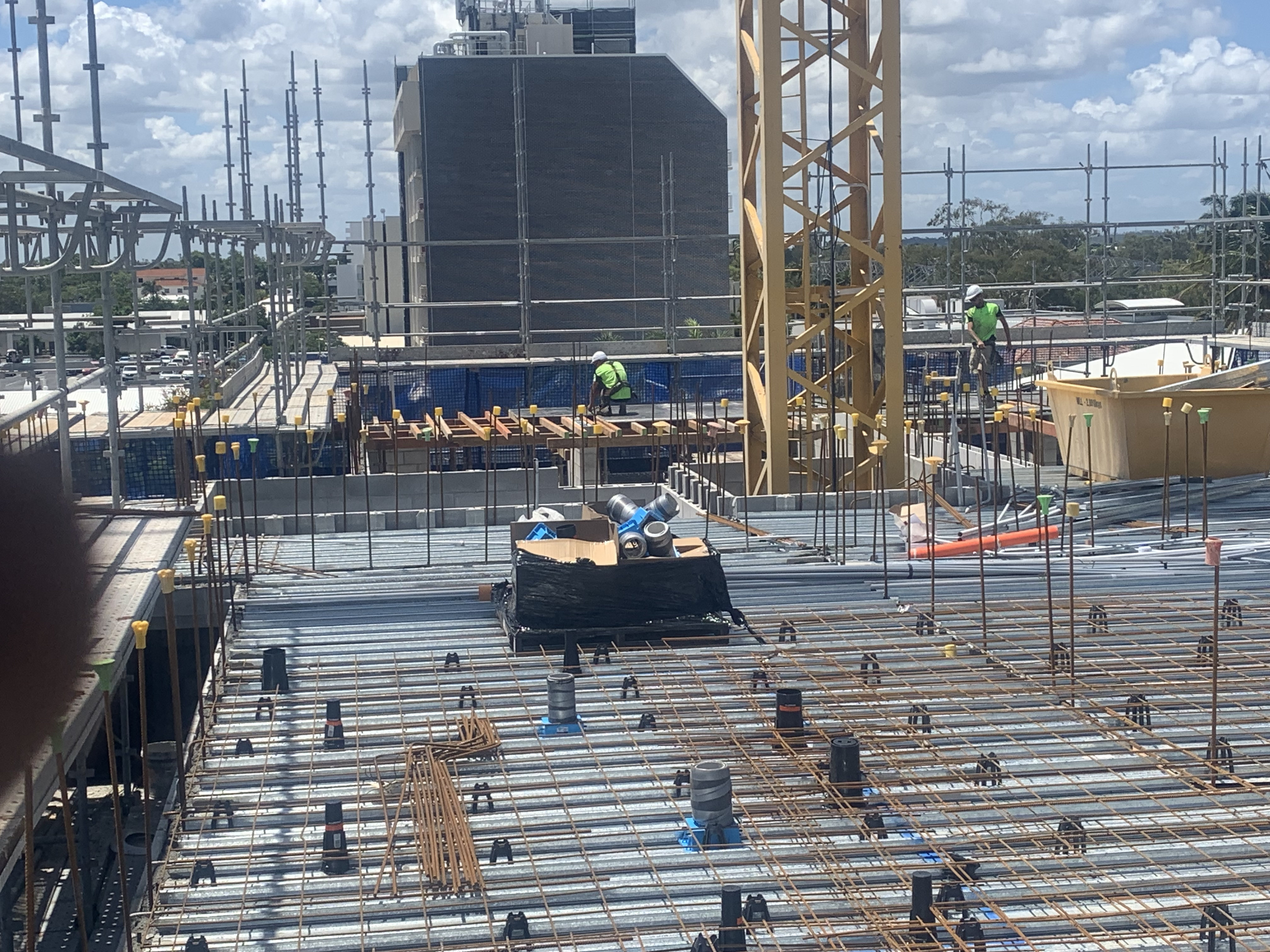 Workers on high-rise concrete slab — crane overhead and apartment towers in background