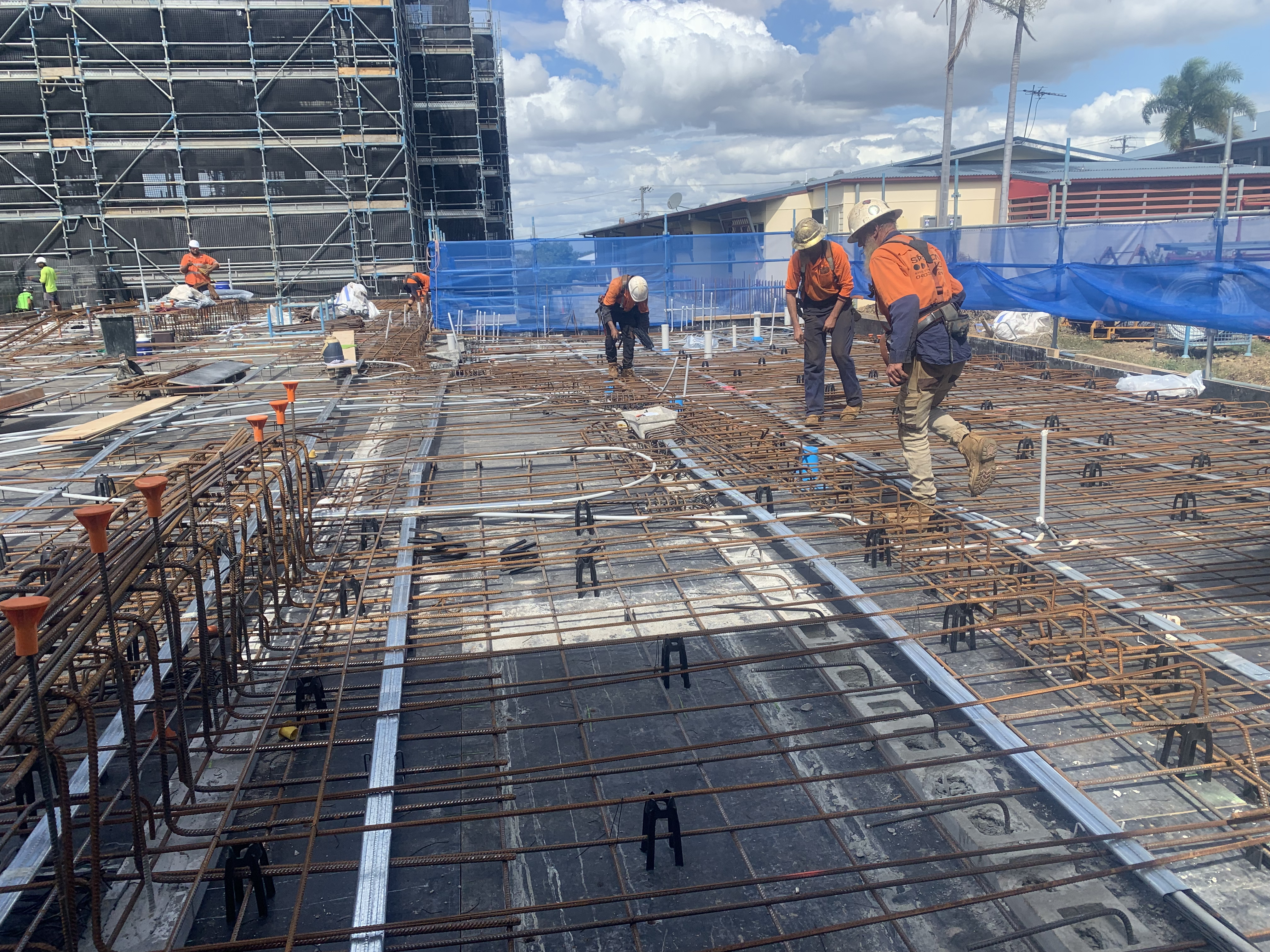 Workers in hi-vis vests preparing reinforcement mesh on a concrete slab