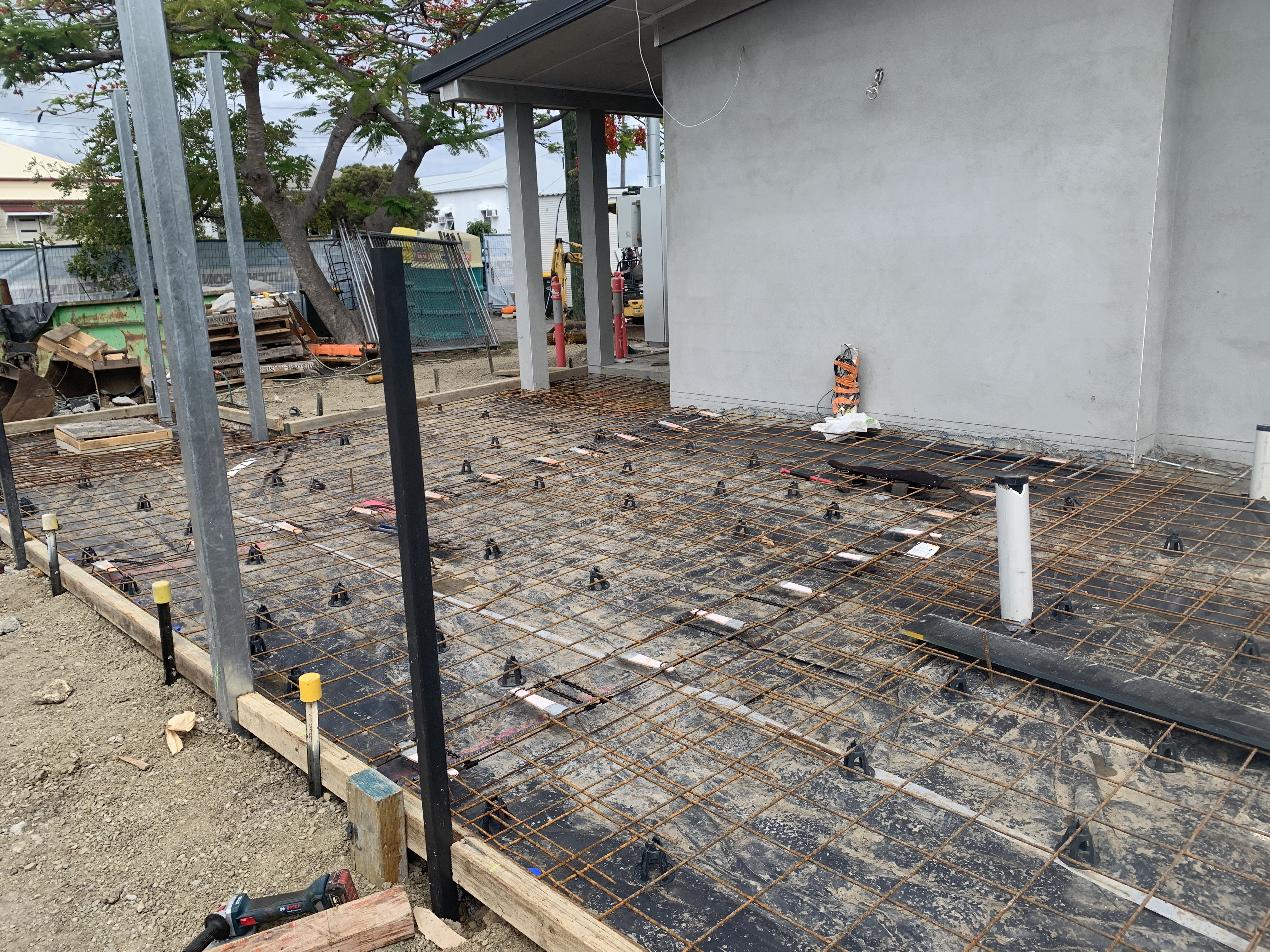 Residential concrete slab preparation — reo mesh and steel posts beside rendered building