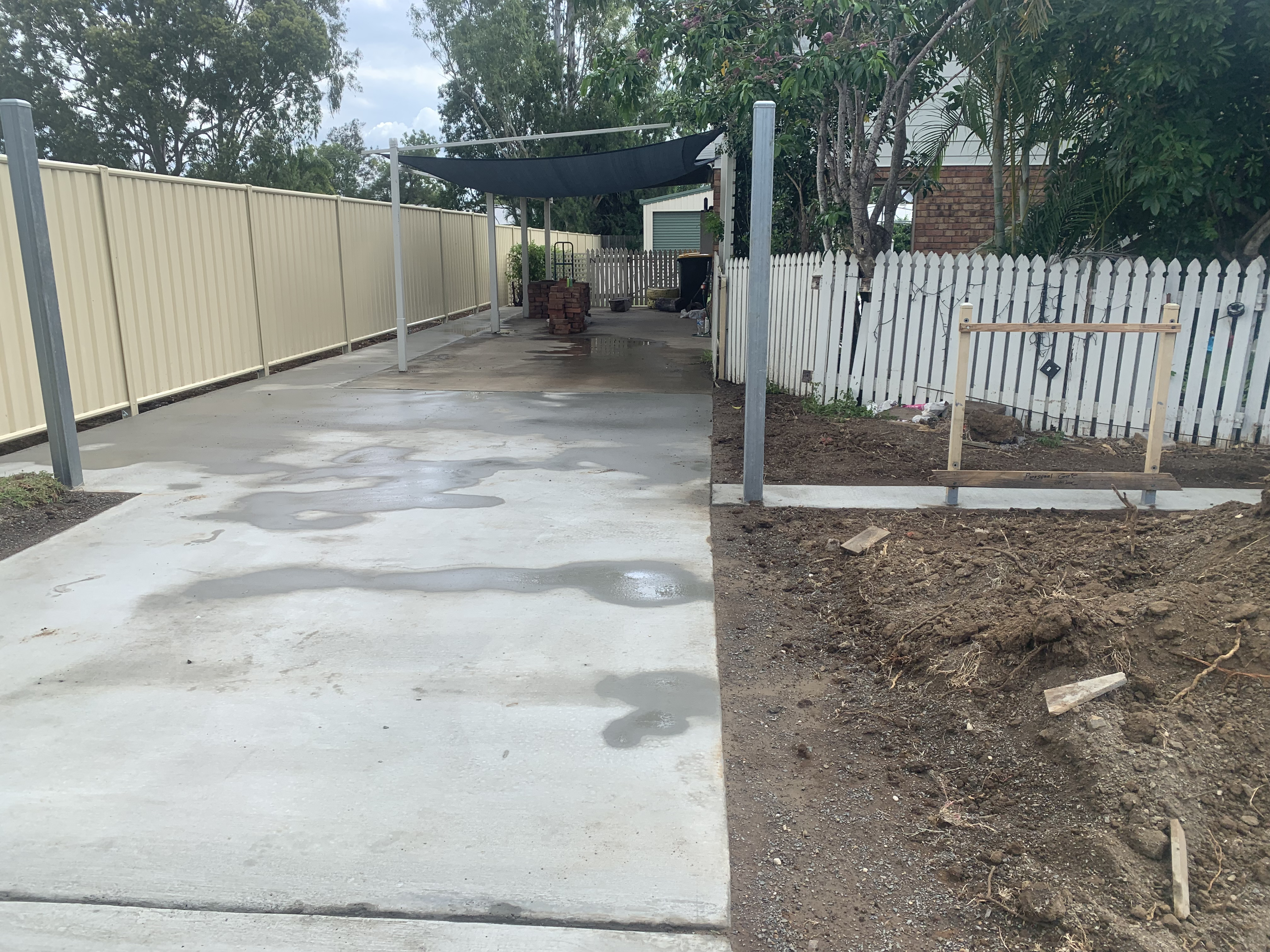 Freshly poured residential concrete driveway and carport beside Colorbond fence