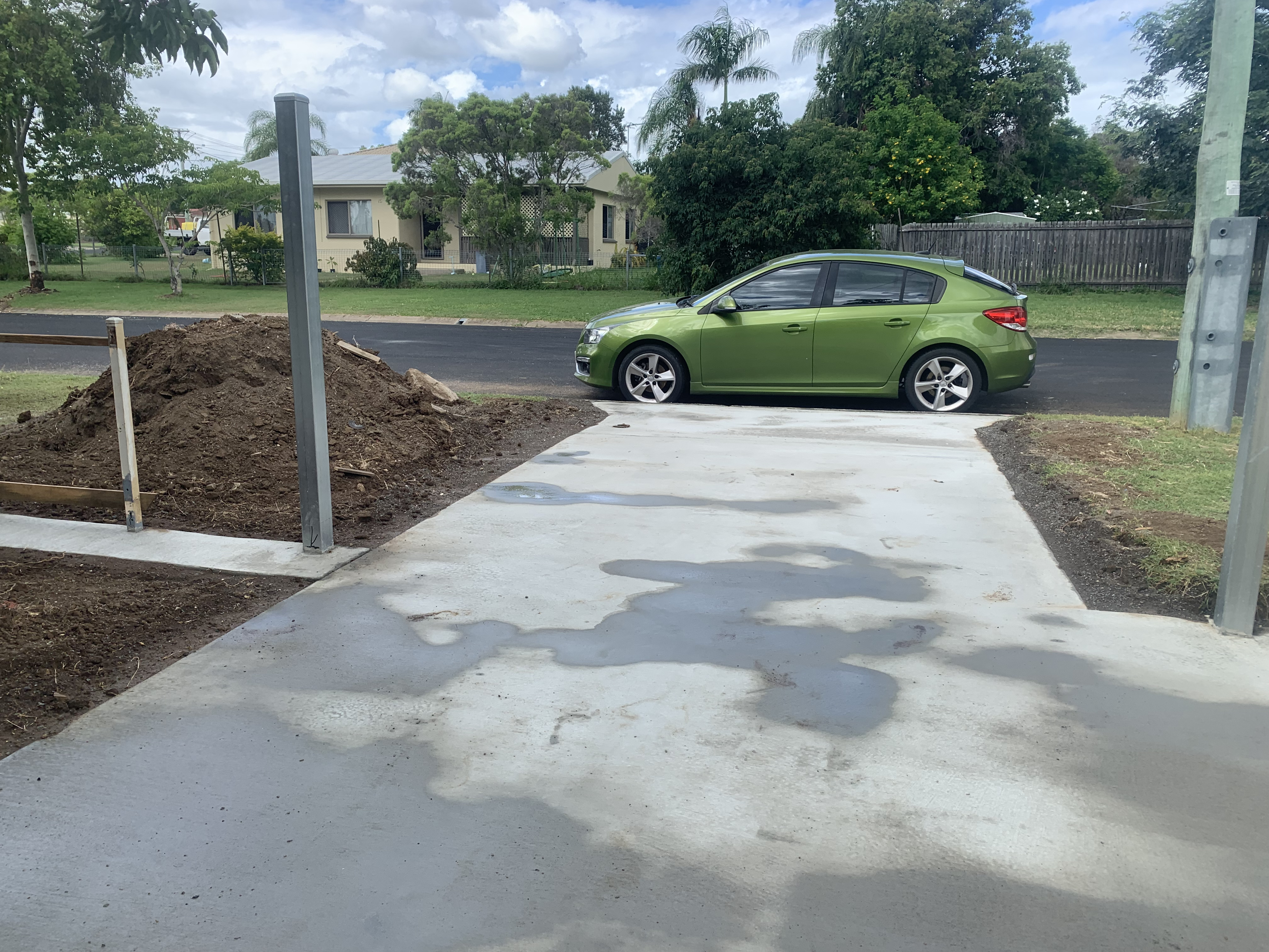 Completed residential concrete driveway viewed from street — fresh pour with soil mound