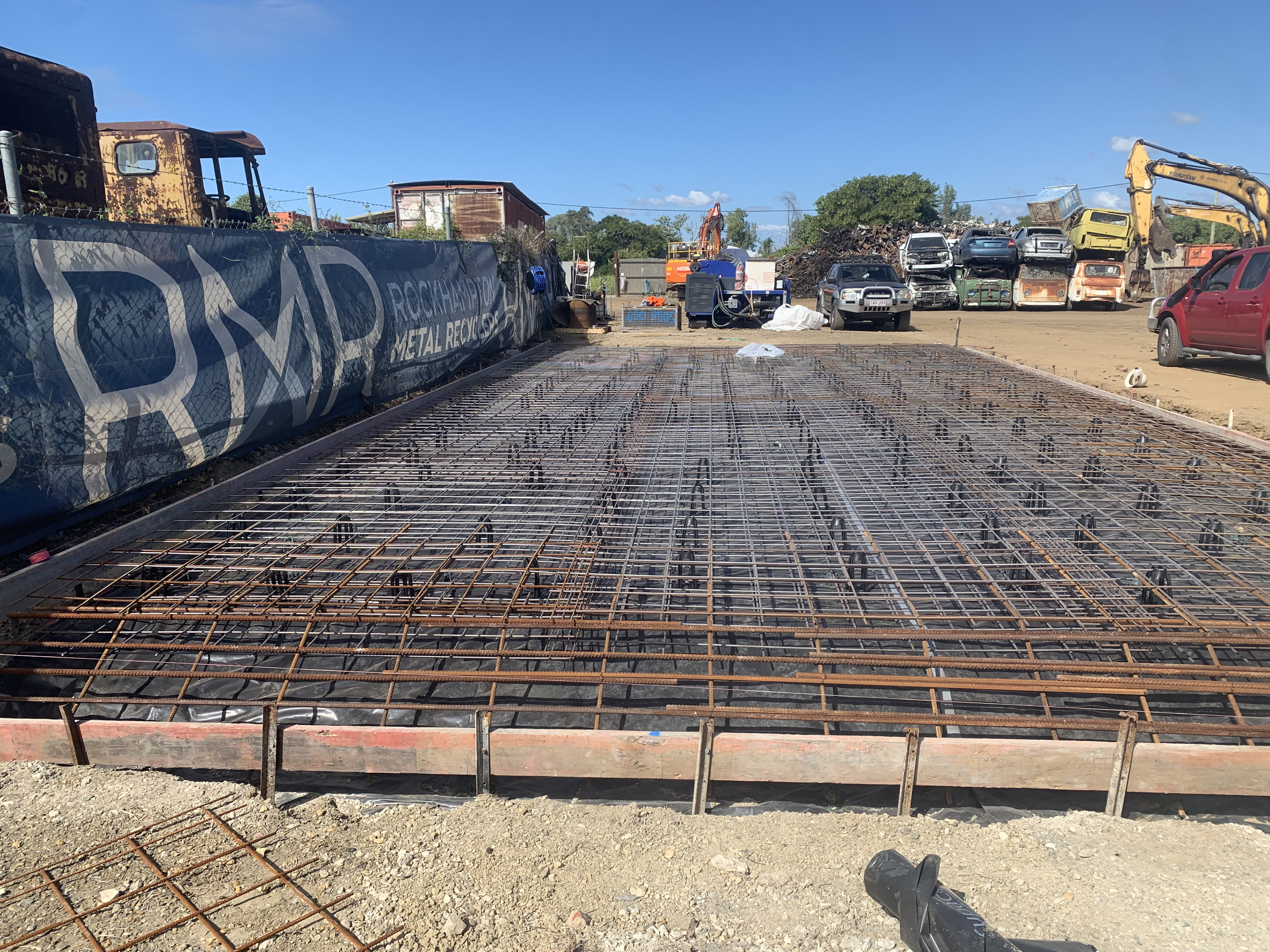 Commercial concrete slab preparation — reo mesh with excavators and trucks in background