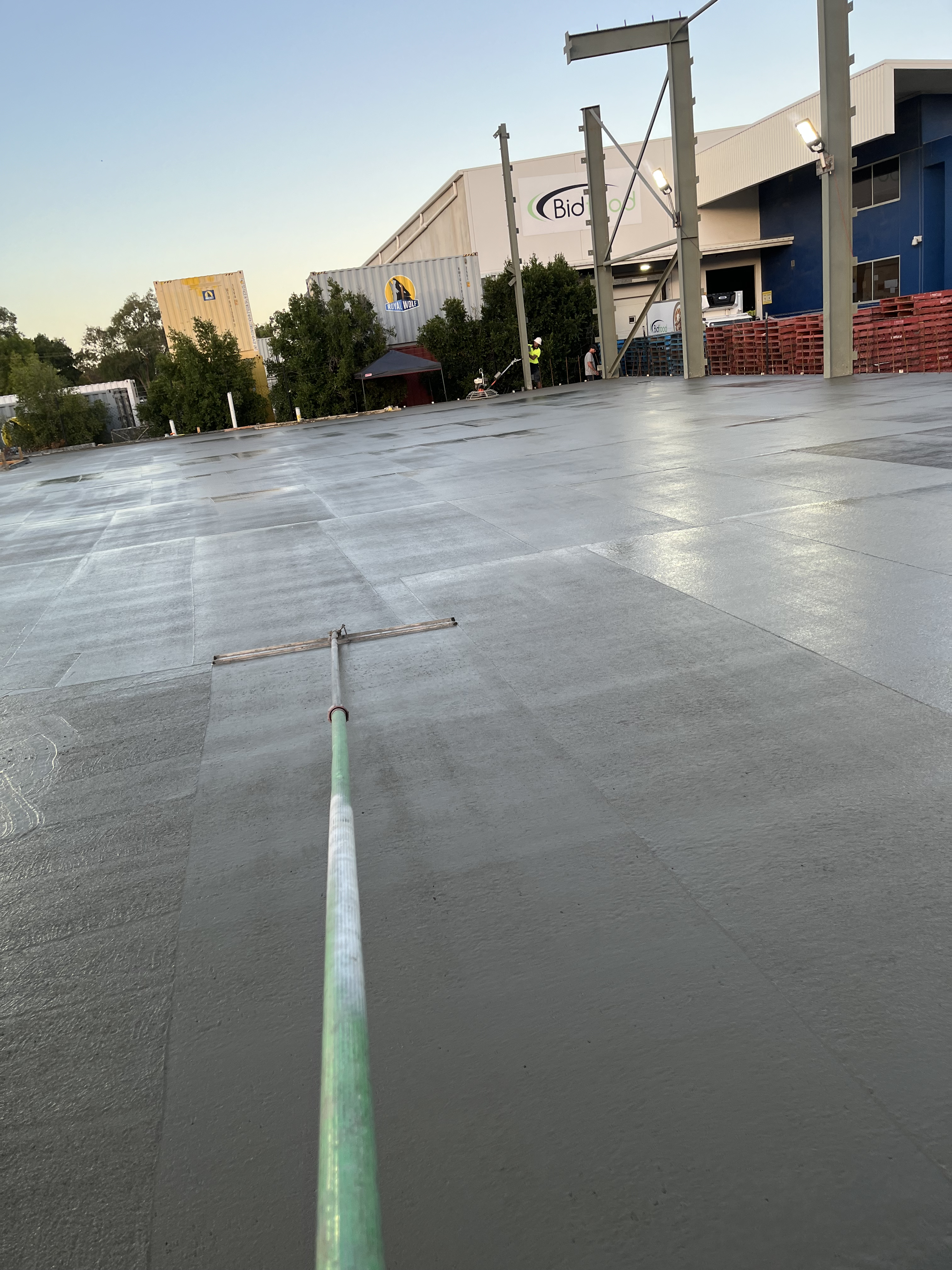Power float on large commercial concrete slab — dusk lighting, buildings in background