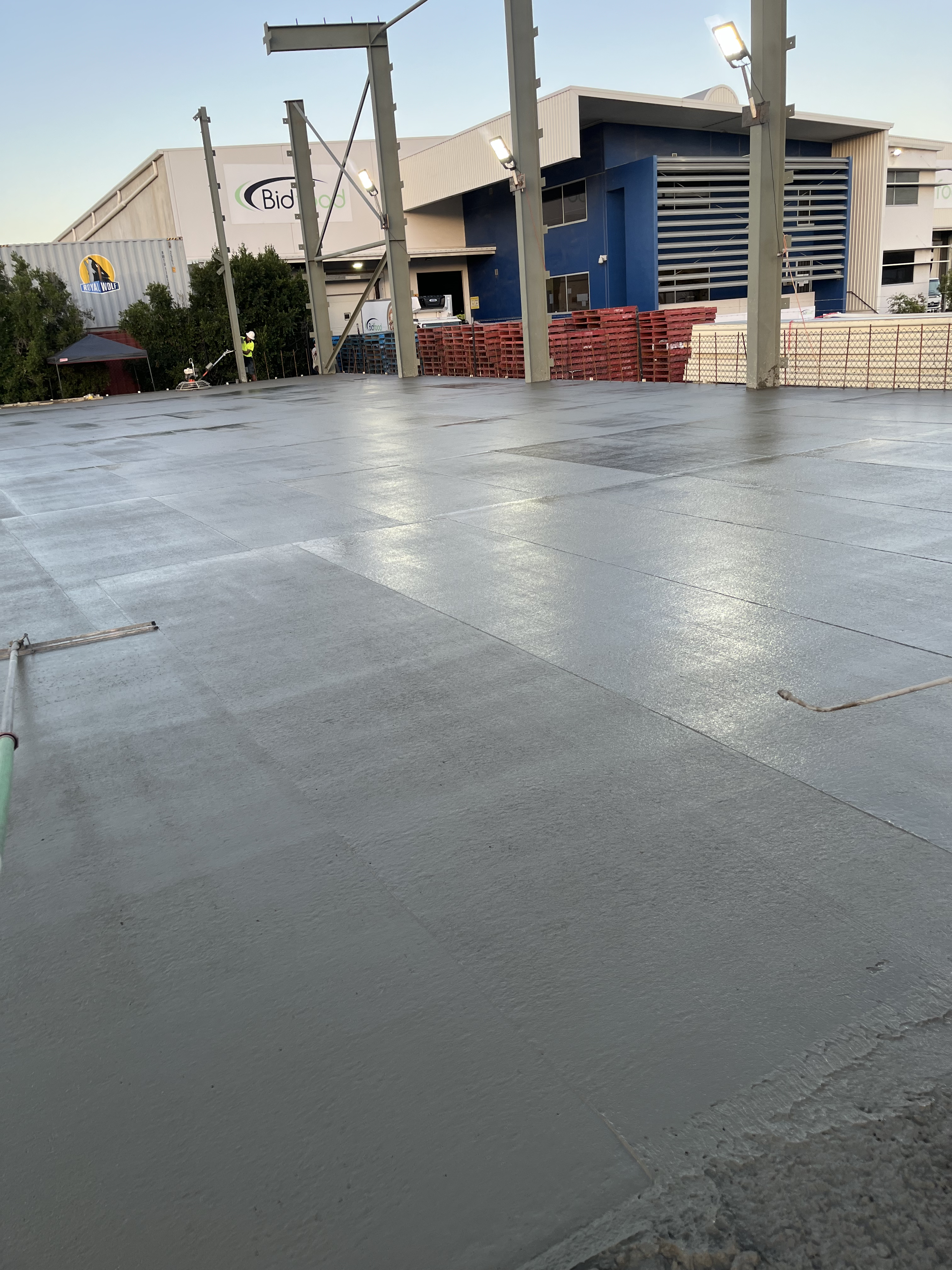 Large commercial concrete slab pour at dusk — joint lines and fresh surface visible