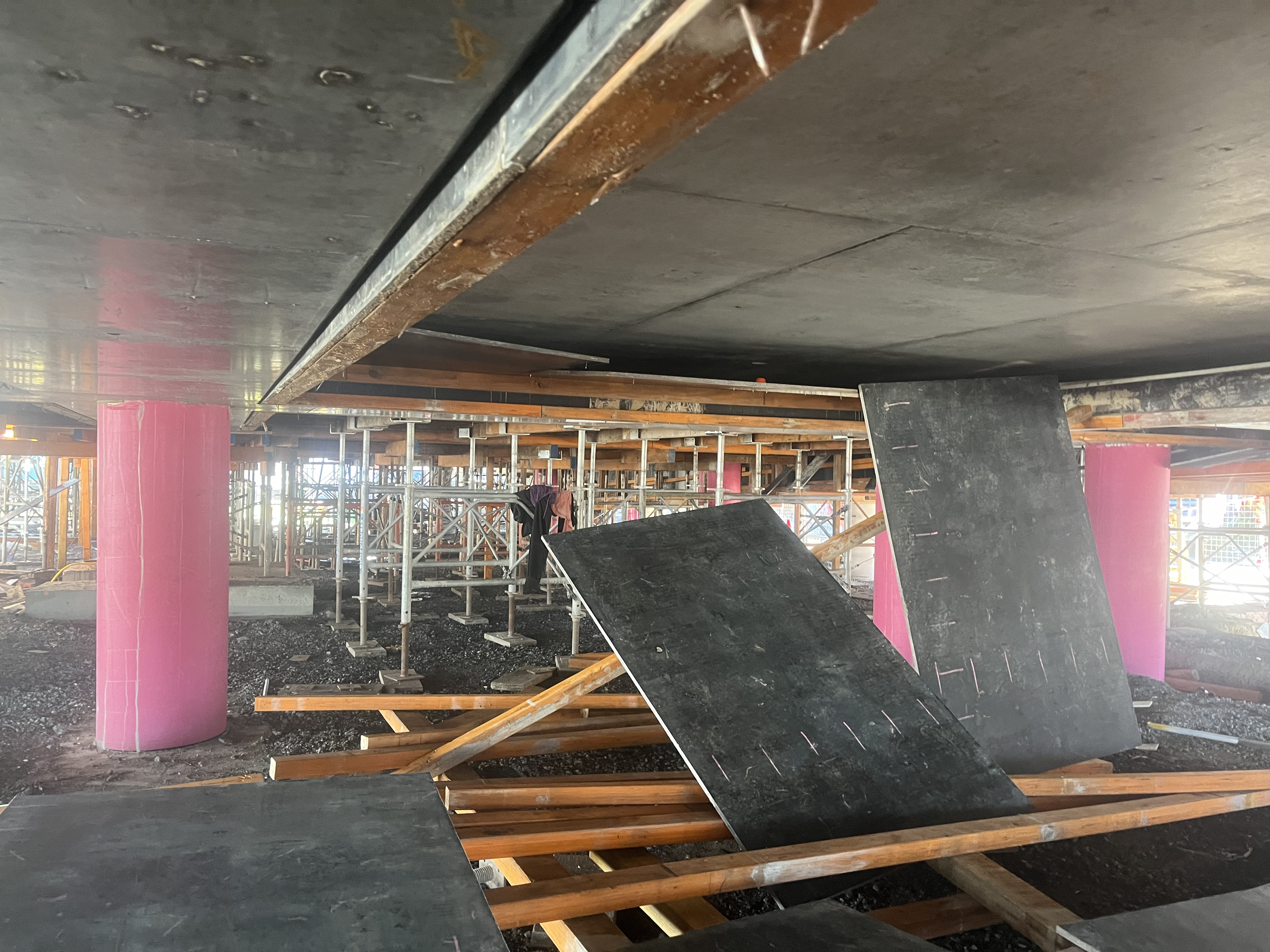 Under-slab perspective — fresh concrete overhead with pink formwork props and worker visible